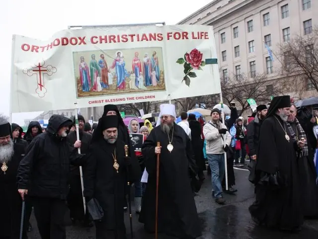 The image shows a group of orthodox Christians marching down a street, holding a banner with text...