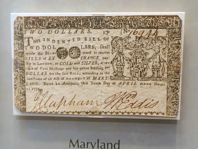The image shows a Maryland two dollar bill from 1774 on display in a glass case. The bill is in the...