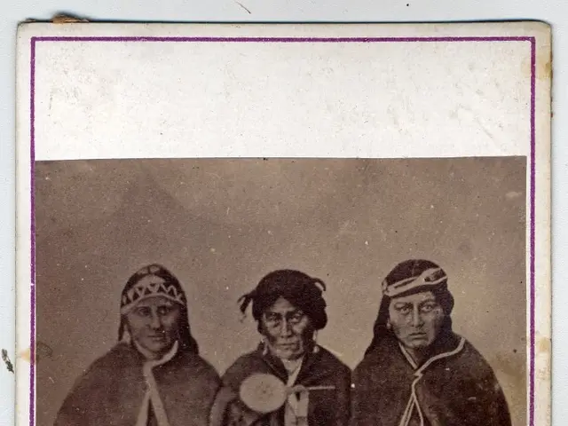 The image shows an old black and white photo of three Native American Indians sitting on a bench....