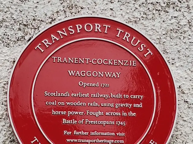 The image shows a red plaque on the side of a building that reads "Transport Trust". The plaque is...