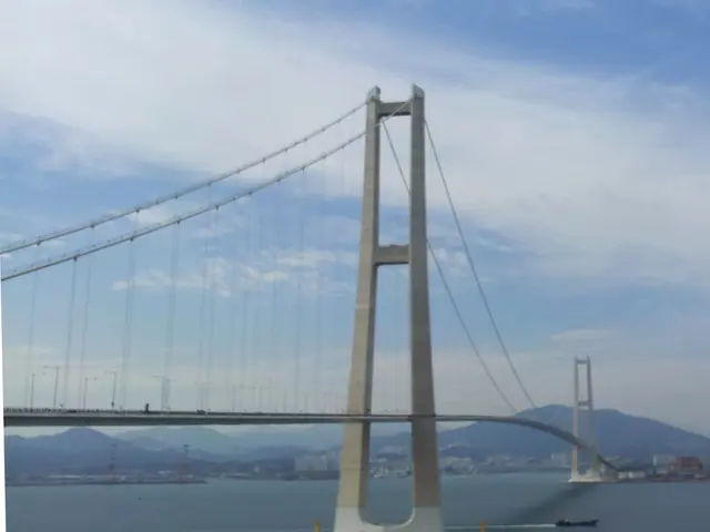 The image shows a large bridge spanning a large body of water, with a boat sailing underneath it....