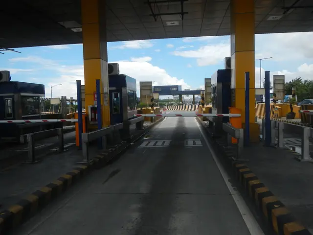 The image shows a toll booth at the entrance to a toll station, with vehicles on the road, barrier...