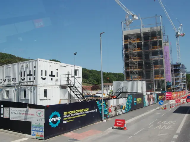 The image shows a construction site with a large building under construction, surrounded by cranes,...