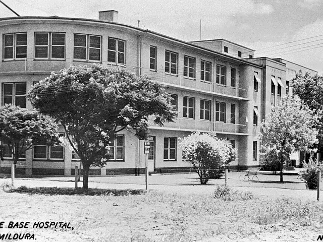 The image shows a black and white photo of the base hospital in Mildura, with trees, plants, poles,...