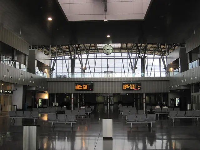 The image shows an empty airport terminal with many empty chairs and tables, dustbins on the floor,...