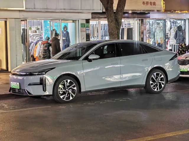 The image shows an electric car parked on the side of a street at night, surrounded by buildings,...