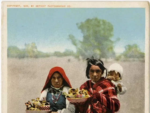 The image shows two Native American women standing on the ground, each holding a basket of fruit in...