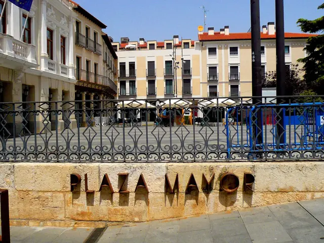 The image shows the Plaza Mayor in Madrid, Spain. It features a wall with text on it, a metal...